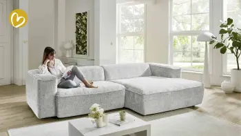 Frau sitzt entspannt auf einem Sofa und ließt ein Möbelmagazin